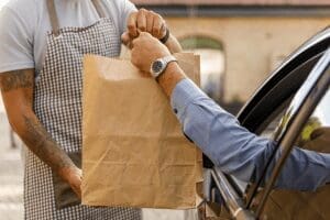 Store employee handing paper bag to man in vehicle