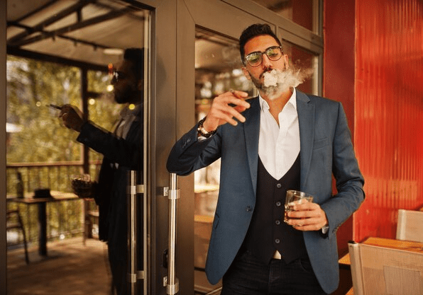 Man holding a glass in one hand and a cigarette in the other as he smokes outside